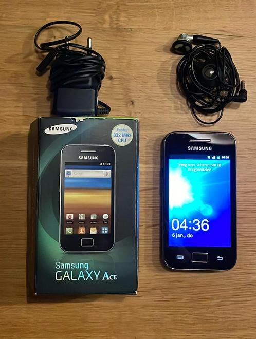 Samsung Galaxy Ace met oplader, oortjes en doosje.